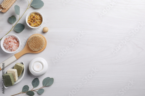 Flat lay composition with different spa products, burning candle and eucalyptus branches on light wooden table. Space for text