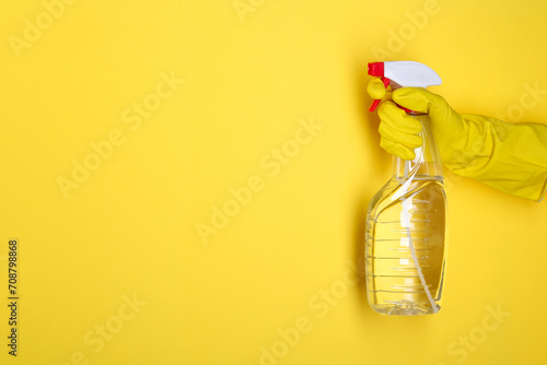 Woman holding plastic spray bottle on yellow background, closeup. Space for text photo