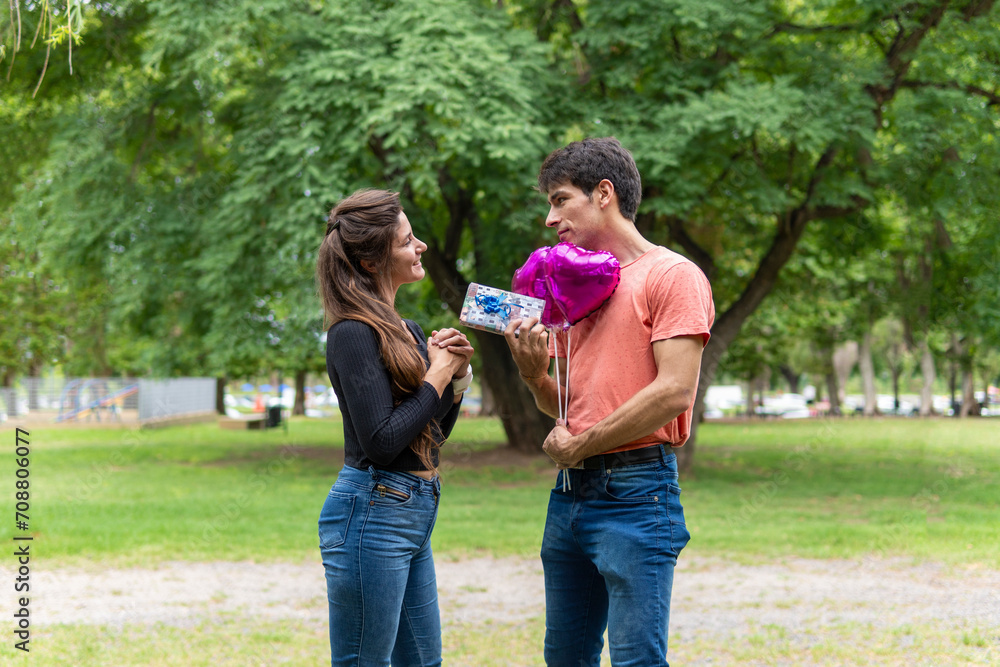 Fototapeta premium Man giving gift to girlfriend, with heart-shaped balloon.