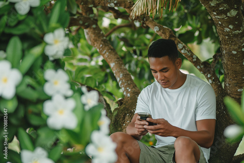 Young Man Using Smartphone While Sitting Under a Flowering Tree in a Park During Daytime © Margaret