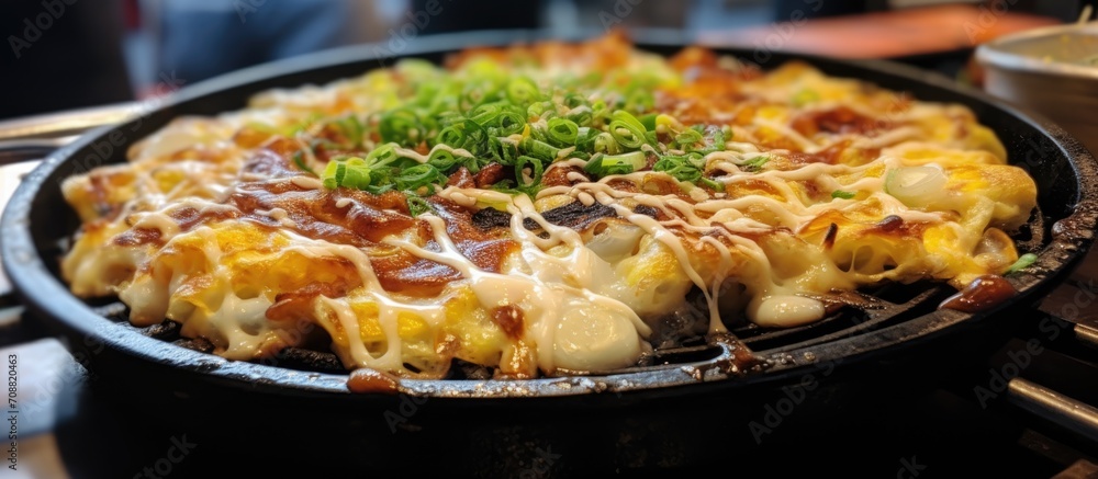 Popular street food in Osaka, Japan, is the delicious Okonomiyaki, a savory pancake made with flour, vegetables, and noodles on a sizzling teppanyaki pan.