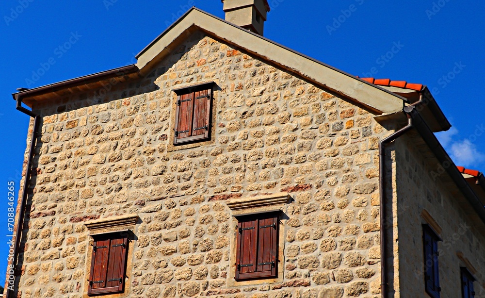 Stone house with windows closed with wooden shutters against a blue sky