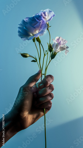 A hand gently grasps delicate flowers against a serene blue backdrop  symbolizing grace and the fleeting nature of beauty