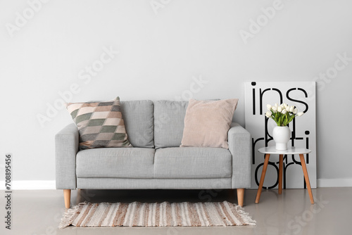 Cozy sofa with cushions and tulip flowers in vase on table near grey wall © Pixel-Shot