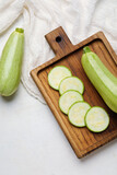 Wooden board with cut and whole zucchini on light background