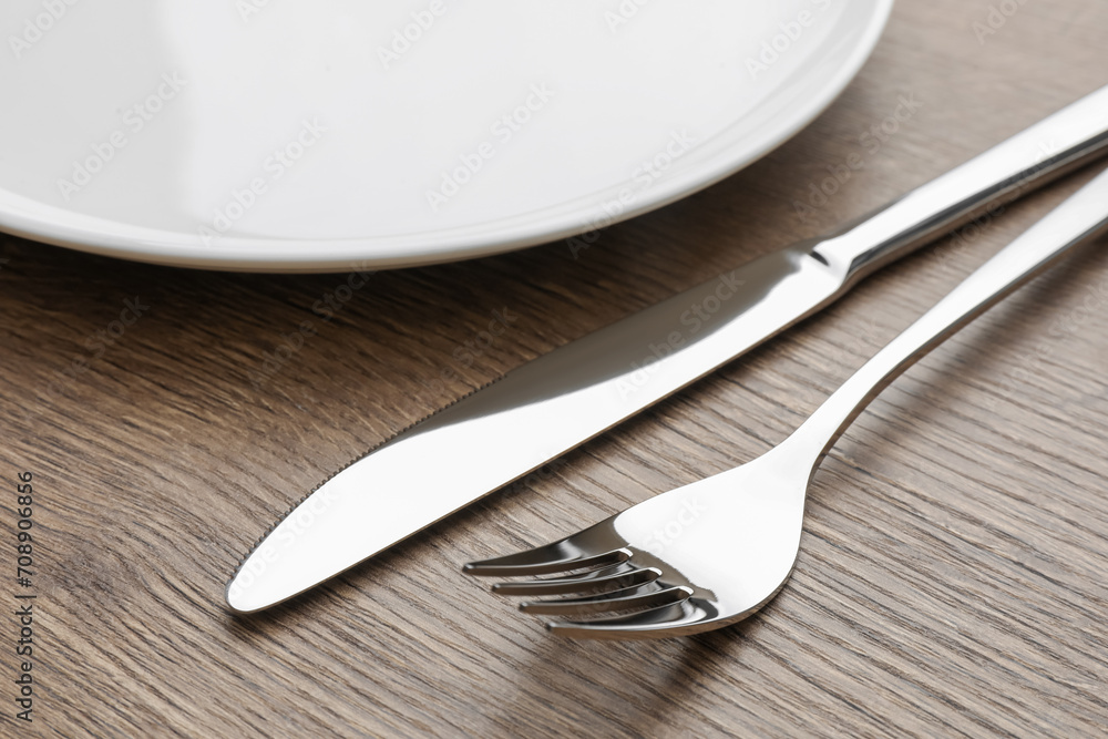 Plate, fork and knife on wooden table, closeup Plate, fork and knife on wooden table, closeup