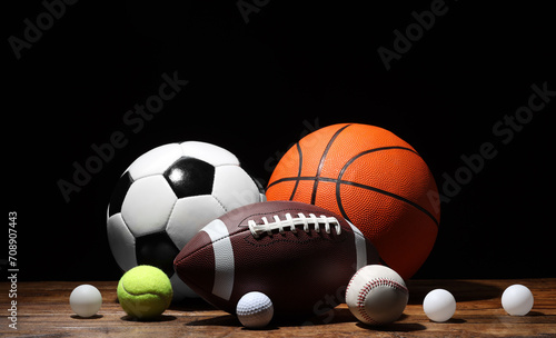 Many different sport balls on wooden table against black background