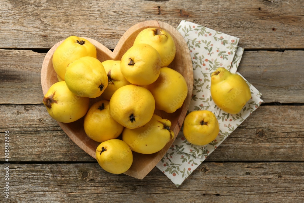 Tasty ripe quinces in heart shaped bowl on wooden table, top view