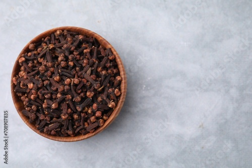 Aromatic cloves in bowl on gray table, top view. Space for text