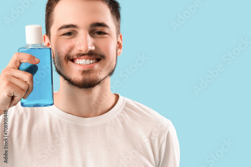 Handsome young man with bottle of mouthwash on blue background. Dental care concept photo