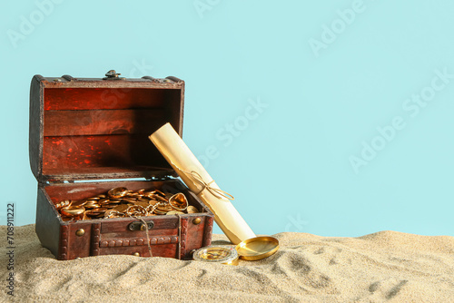 Old chest with treasures , map and compass on sand against blue background photo