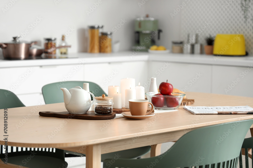 Wooden table with coffee, apples and burning candles in modern kitchen