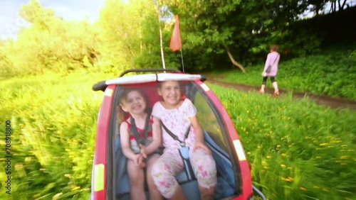 Two little girls ride in trailer along grassy green lawn at park.