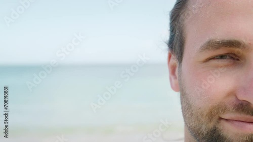 Happy young man with burn skin looking at camera and smiling at the beach during vacation. Cracked, peel off dry skin beauty concept, skincare treatment, cosmetics and sunburn. 4K Slow Motion photo
