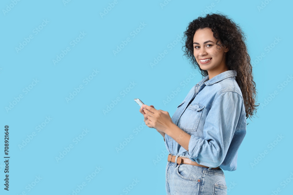 Young African-American woman using mobile phone on blue background