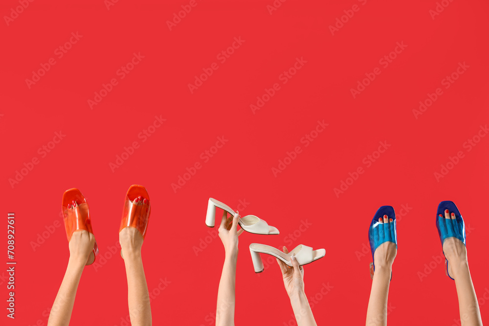 Female hands holding different shoes on red background - obrazy, fototapety, plakaty 