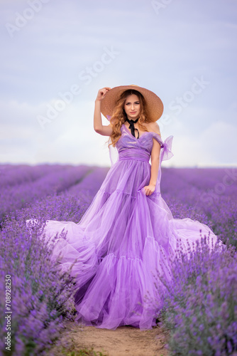 beautiful woman in a lush lilac dress in a field of lavender. She's wearing a big braided hat