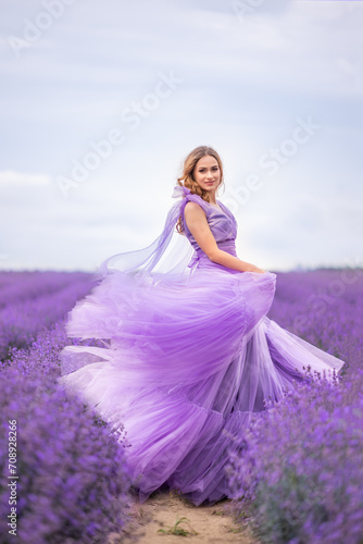 beautiful woman in a lush lilac dress shining from the wind in a field of lavender.