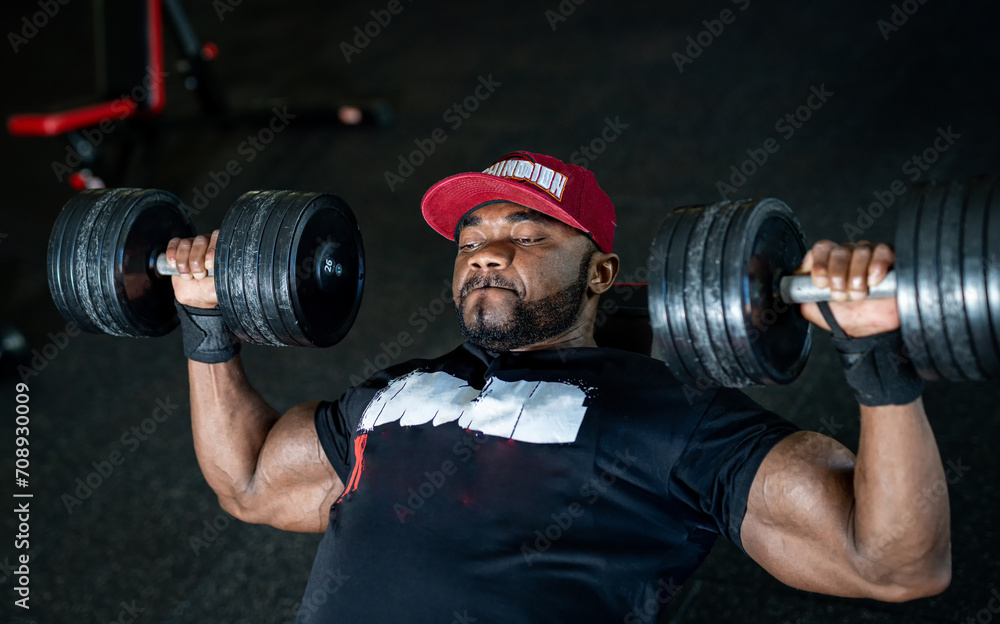 Muscular black guy training hard in gym. Bodybuilding man workout with barbells.