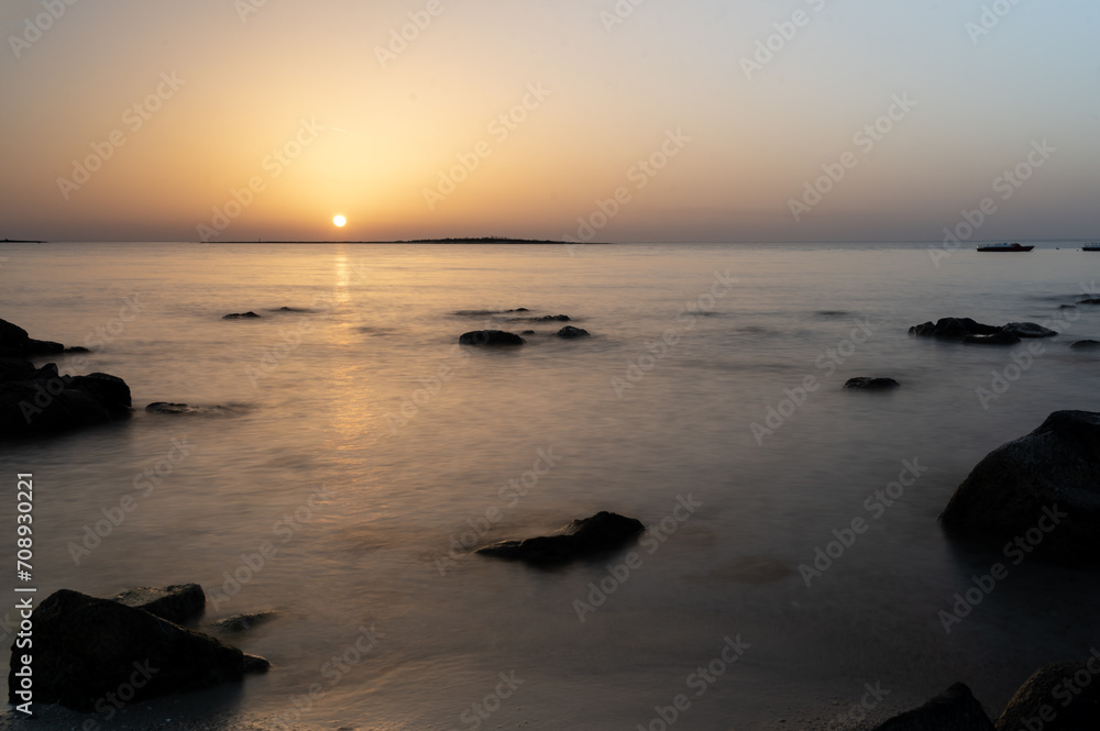Tramonto sul mare con il mare effetto seta, gli scogli ed il riflesso del sole sull'acqua. 