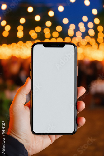 Smartphone with blank screen in hand on bokeh background .