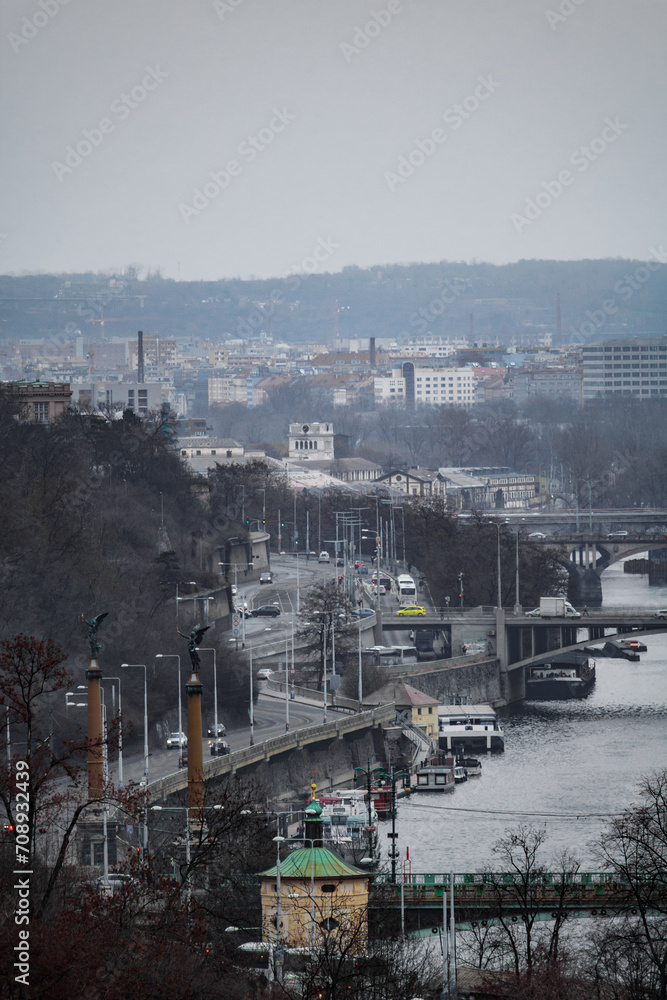 A cityscape view of the of the historic old medieval city of Prague. There re bridges with traffic and the river Vltava