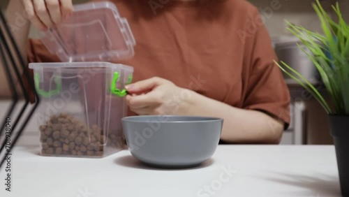 dosage of pet food, the owner measures out a portion of feed for the dog, pours cat food into a bowl from the container at home in the kitchen photo