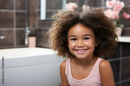Beautiful cute little african american girl in bathrobe relaxing on bed at home after shower, cheerful black kid enjoying spa beauty treatments, smiling and looking at camera, copy space.