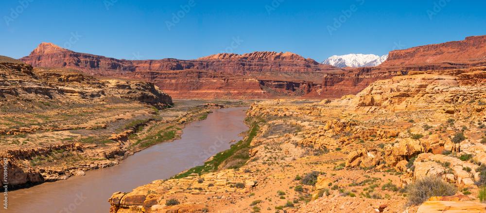 Colorado river in southern Utah, USA, with snow capped mountains in the background. Arid terrain, desertic area, deep blue sky.