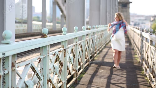 Pretty pregnant woman in white with scarf walks on railway bridge photo