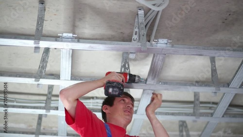 man in uniform install framework for hung ceiling by screwdriver photo