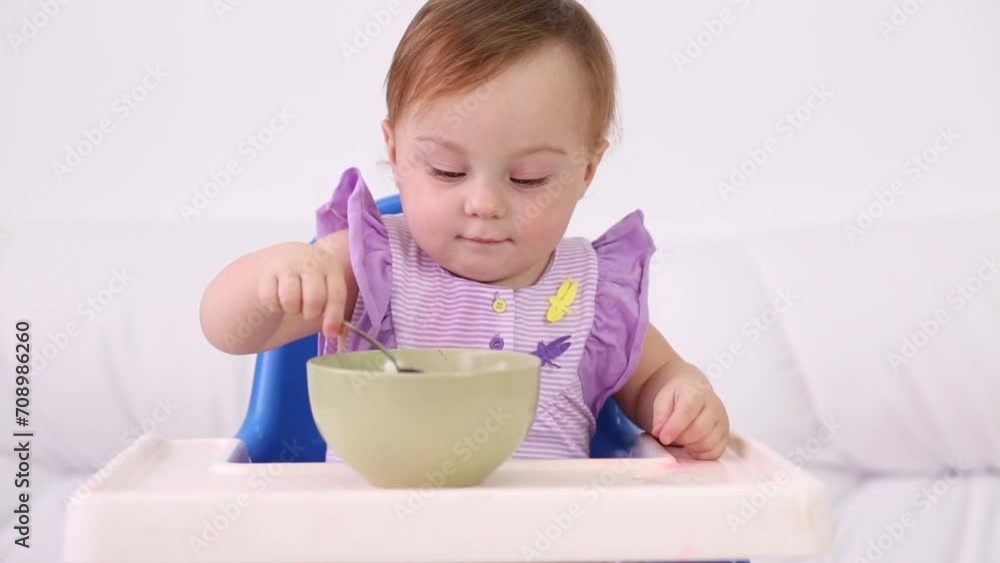 Little smiling baby sits at highchair and eats porridge on plate Little smiling baby sits at highchair and eats porridge on plate
