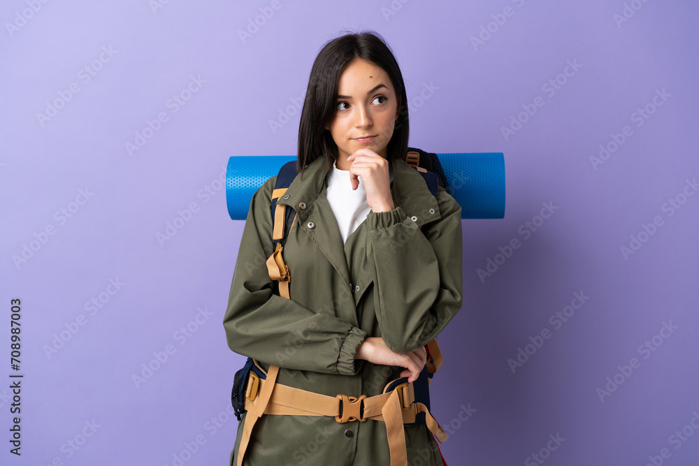 Young mountaineer woman with a big backpack over isolated background and looking up Young mountaineer woman with a big backpack over isolated background and looking up