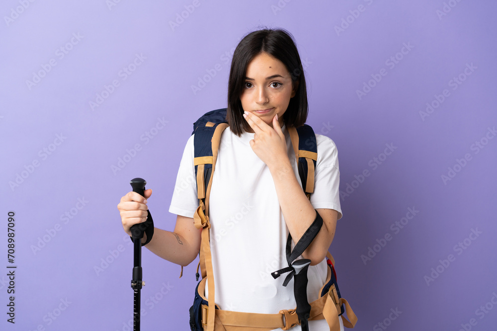 Young caucasian woman with backpack and trekking poles isolated on blue background thinking