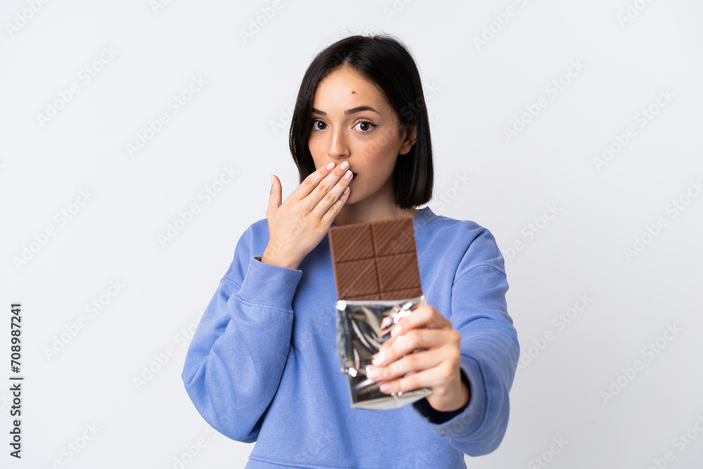 Young caucasian woman isolated on white background taking a chocolate tablet and surprised Young caucasian woman isolated on white background taking a chocolate tablet and surprised
