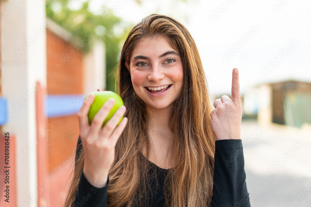 Young pretty caucasian woman with an apple at outdoors pointing up a great idea Young pretty caucasian woman with an apple at outdoors pointing up a great idea
