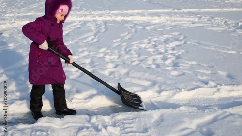 Girl removes snow by shovel for making path at winter