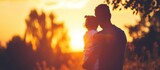 Father embraces daughter in silhouette, playing at sunset in park during vacation.