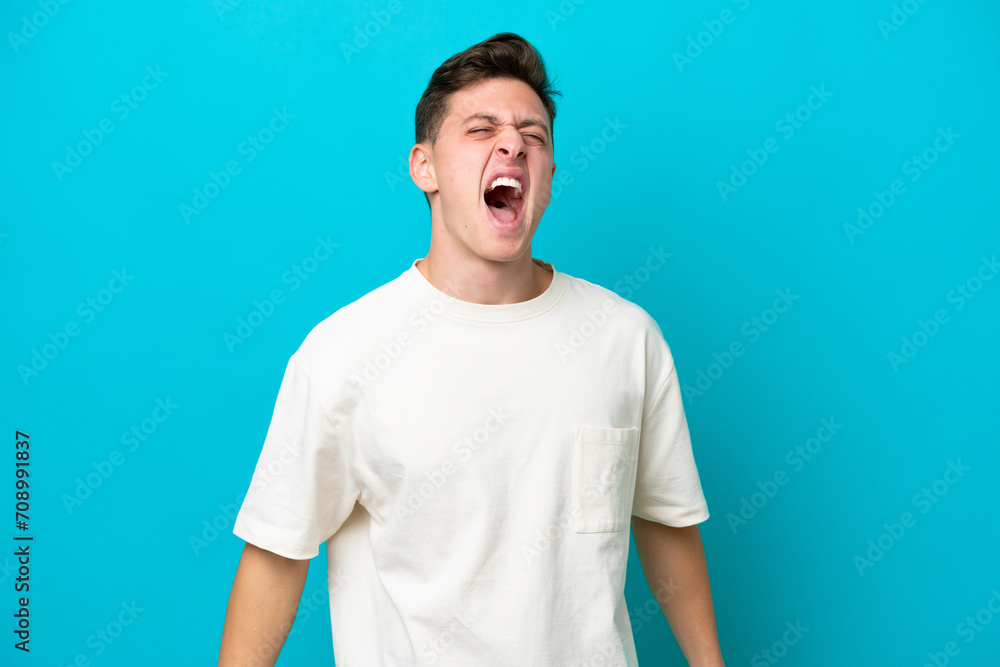Young handsome Brazilian man isolated on blue background shouting to the front with mouth wide open Young handsome Brazilian man isolated on blue background shouting to the front with mouth wide open