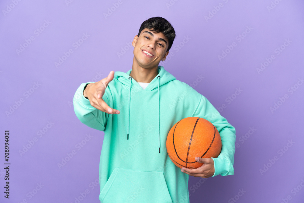 Young man playing basketball over isolated purple background shaking hands for closing a good deal