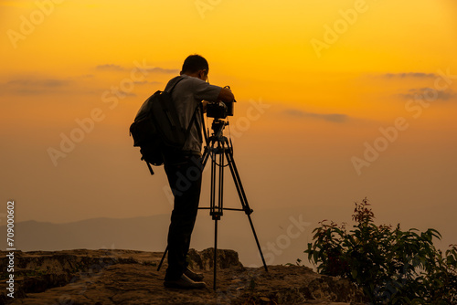 Man photographer on the cliff of the mountain on sunset background