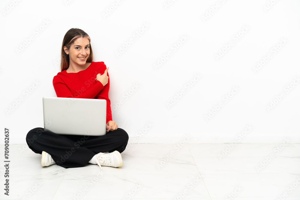 Young caucasian woman with a laptop sitting on the floor pointing back Young caucasian woman with a laptop sitting on the floor pointing back