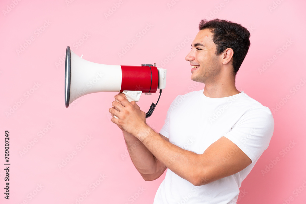 Young caucasian man isolated on pink background shouting through a megaphone to announce something Young caucasian man isolated on pink background shouting through a megaphone to announce something