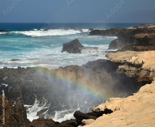 Waves crashing against the rocks and small rainbow, west coast of Jandia, south of Fuerteventura, Canary Islands