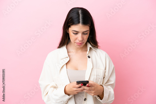 Young Italian woman isolated on pink background using mobile phone