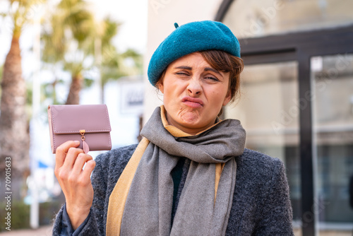 Brunette woman holding a wallet at outdoors with sad expression © luismolinero