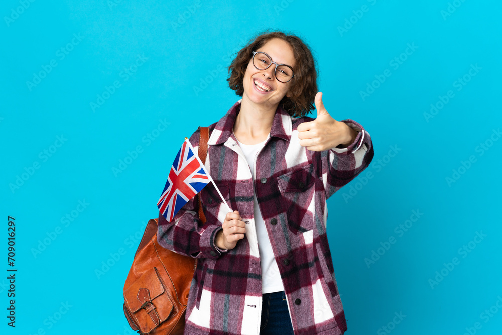 Young English woman holding an United Kingdom flag isolated on blue background with thumbs up because something good has happened Young English woman holding an United Kingdom flag isolated on blue background with thumbs up because something good has happened