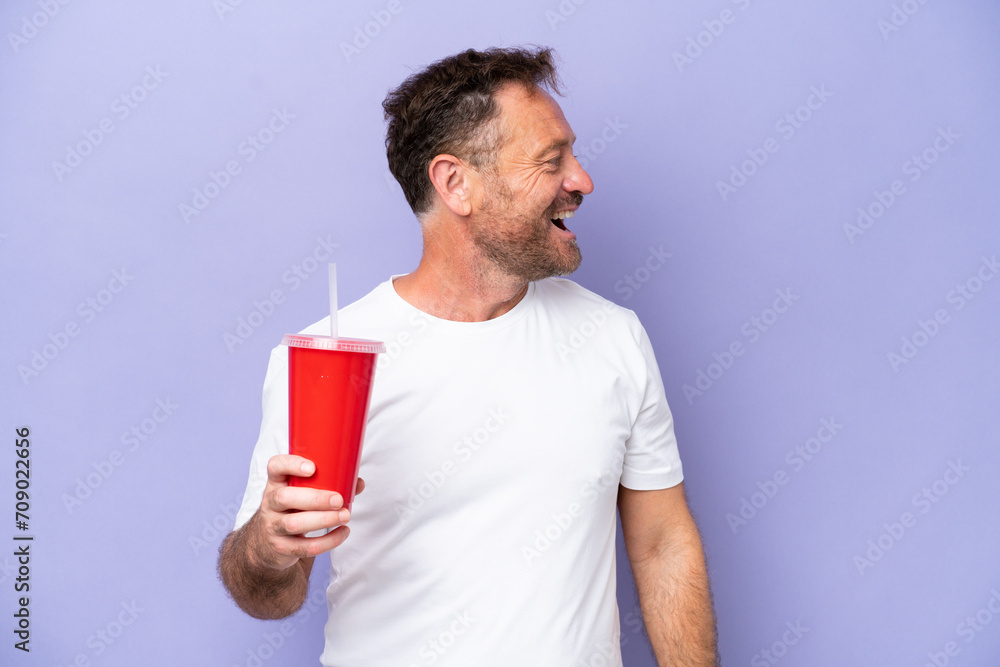 Middle age caucasian man holding soda isolated on purple background laughing in lateral position Middle age caucasian man holding soda isolated on purple background laughing in lateral position