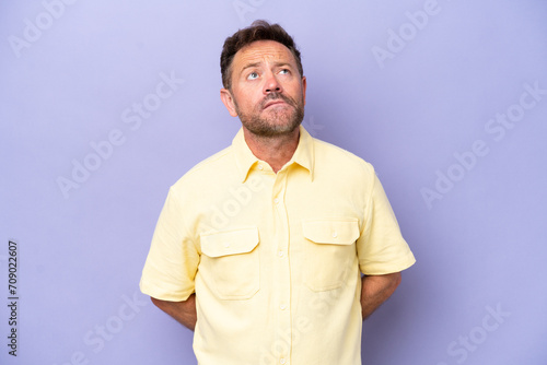 Middle age caucasian man isolated on purple background and looking up © luismolinero