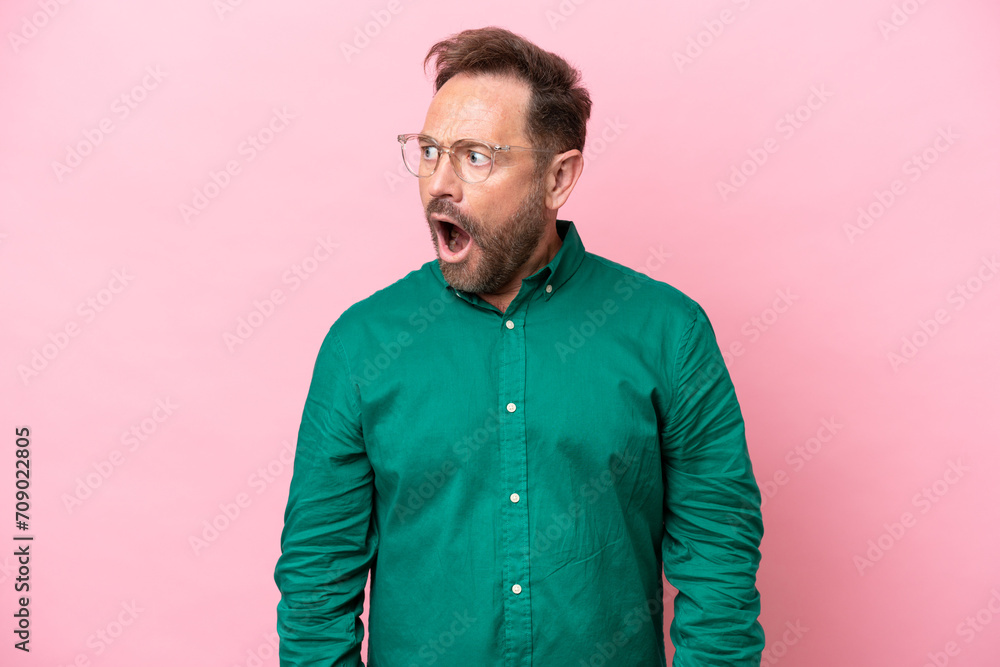 Middle age caucasian man isolated on pink background doing surprise gesture while looking to the side Middle age caucasian man isolated on pink background doing surprise gesture while looking to the side
